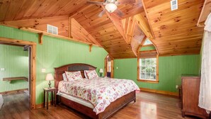 A spacious bedroom with a wooden ceiling, a large bed, a nightstand, a dresser, and a window with a view of trees. - 3 BR/3.5 BA w/ Hot Tub & 12 min drive to Ash Cave (New Plymouth)