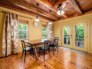 Une salle à manger en bois, avec une table et des chaises en bois, un ventilateur de plafond et une horloge au mur.
