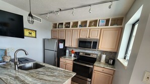 A modern kitchen with a granite countertop, stainless steel appliances, wooden cabinets, and a window with a view.