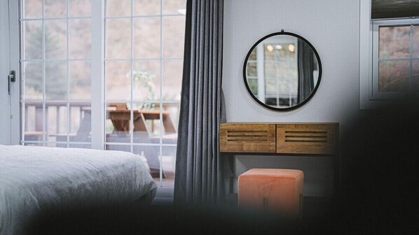 Un dormitorio con cama, cómoda de madera, espejo redondo y ventana con cortinas.