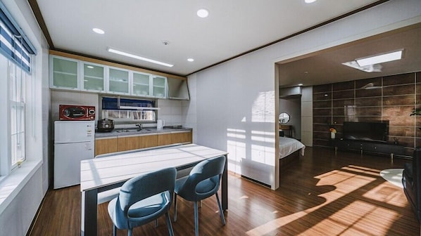 A modern kitchen with a dining area, a TV in the living room, and a large window providing natural light.