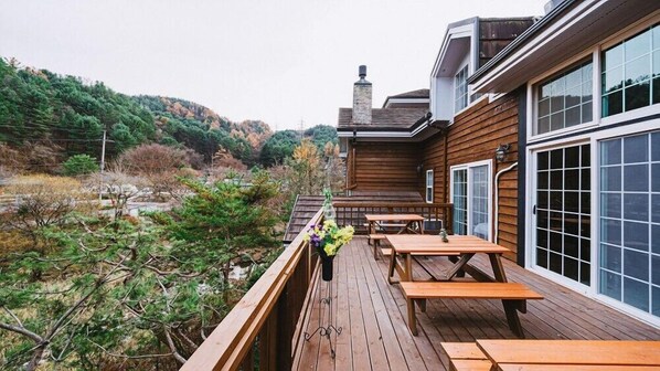 A wooden deck with picnic tables overlooking a forested hillside. - Pension Irum (Gapyeong)