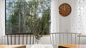 En matplats med ett bord, stolar, en vas med gröna växter, en klocka och ett fönster med utsikt över en skog.