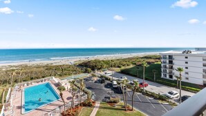 Une piscine avec vue sur la plage, un parking et un immeuble doté de balcons.