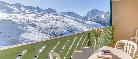 Een balkon met uitzicht op besneeuwde bergen, een ronde tafel met stoelen en een vaas met bloemen.