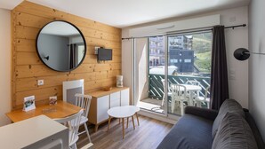 Una habitación moderna con pared de madera, un espejo redondo, un televisor, una mesa de comedor con sillas, un sofá y un balcón con vistas a edificios.