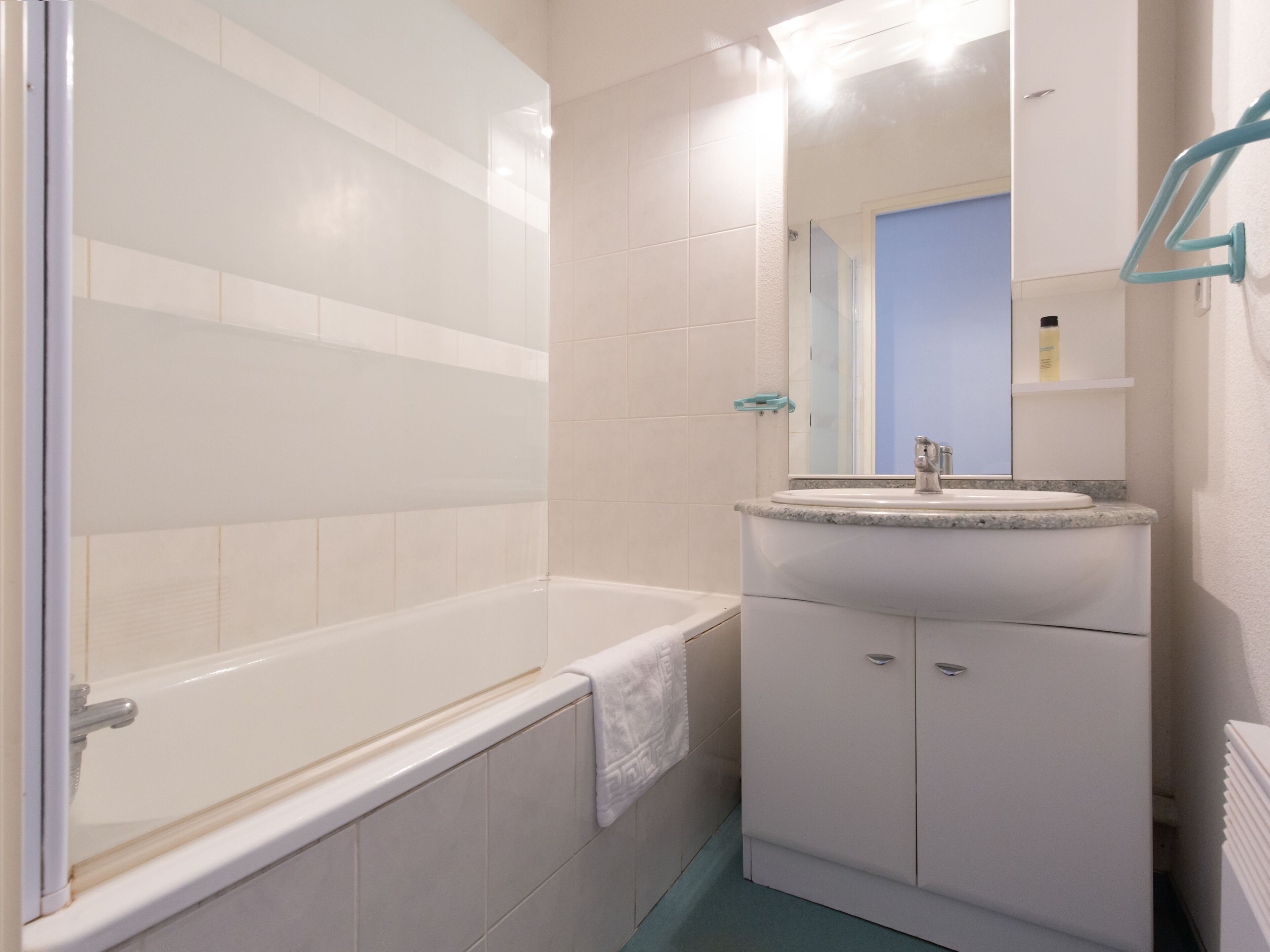 Een badkamer met een bad, een wastafel met spiegel en een handdoek aan de muur.