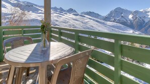 Een terras met een tafel en stoelen, een vaas met bloemen en uitzicht op besneeuwde bergen.