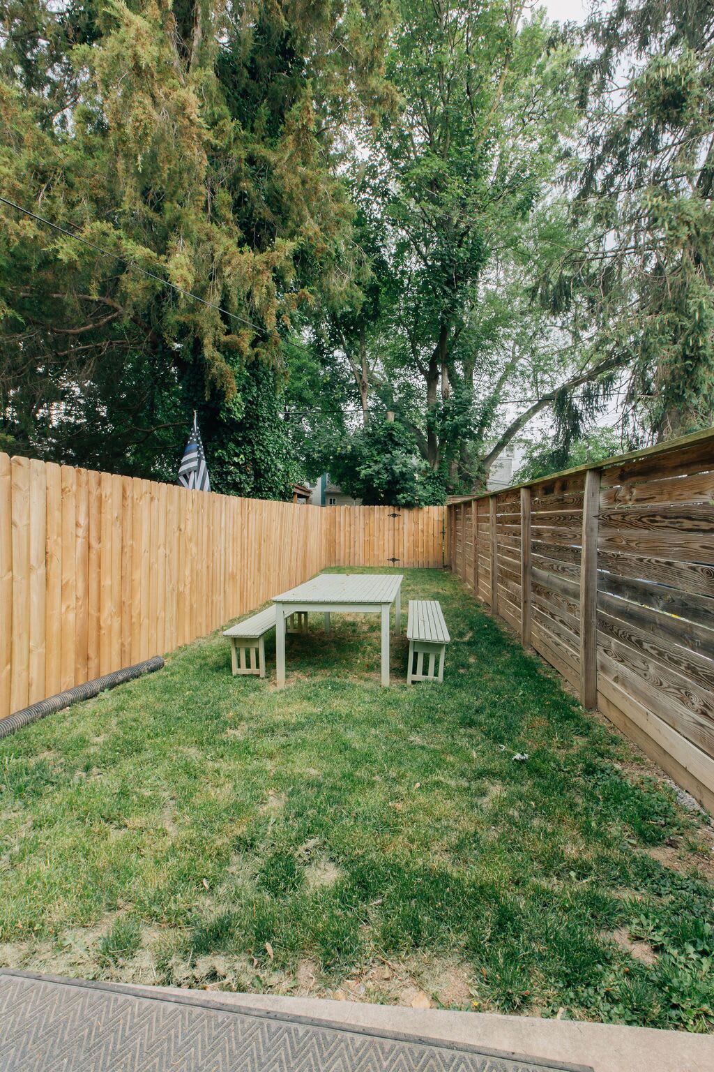 Un cortile con recinzione in legno, un tavolo da picnic e una panchina.