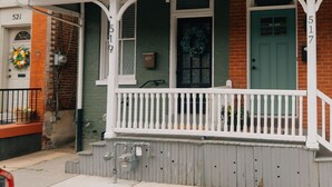 Une maison de ville à deux étages, dotée d’une façade verte, de boiseries blanches et d’un porche avec une balustrade blanche.