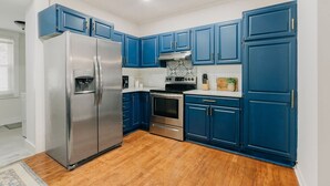 Une cuisine avec des meubles de couleur bleue, des appareils électroménagers en acier inoxydable et un plancher en bois.