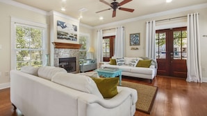A spacious living room with a fireplace, white sofas, a coffee table, and large windows with curtains. - "Will O Mist" - Inlet Beach Home, Bikes, Pool, Dock (Inlet Beach)