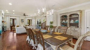 Un coin repas avec une table en bois, des chaises et un lustre. Un escalier mène à un autre niveau, et il y a une vitrine contenant des objets décoratifs.