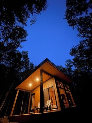 A modern house with a large glass door, a wooden deck, and a view of the sky. - Tanières Microchalets (Baie-St-Paul)