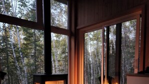 Um quarto acolhedor com lareira a lenha, grandes janelas e cama com roupa de cama estampada.