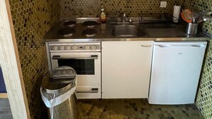 A compact kitchen with wooden cabinets, a stainless steel stove, a sink, and a small refrigerator.