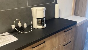 A modern kitchen with a coffee maker on the counter, a paper towel holder, and a white toilet in the background.