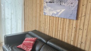 A living room with a black leather sofa, a wooden paneled wall, and a winter-themed painting.