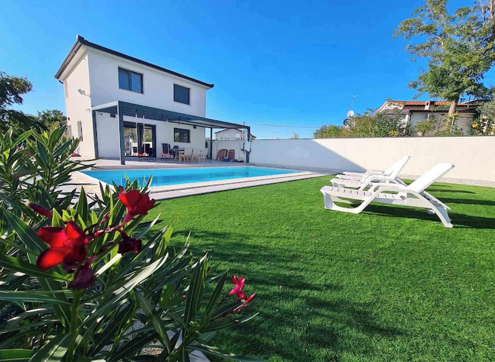 Een modern huis met twee verdiepingen, een zwembad, een overdekt terras en een verzorgd gazon.