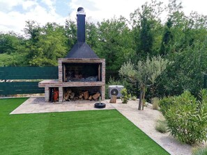 Ein gemauerter Kamin im Freien mit Schornstein, umgeben von gepflegtem Rasen und viel Grün.