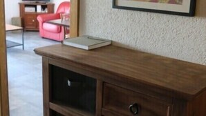 A wooden cabinet with drawers and a flat surface, a framed abstract painting on the wall, and a red chair in the background.
