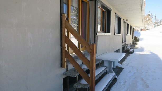 A snow-covered outdoor area with a wooden staircase leading to a building entrance.