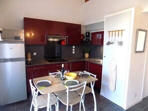 Uma cozinha compacta com armários vermelho escuro, forno embutido e mesa de jantar para quatro pessoas.