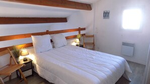 A bedroom with a wooden headboard, a bed with white bedding, a nightstand with a lamp, a chair, and a radiator.