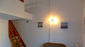 A room with a wicker sofa, a staircase, and wall-mounted artwork.