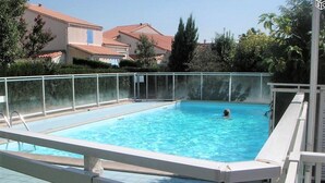 A rectangular swimming pool with a white poolside deck and a glass safety fence.