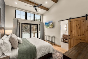 A spacious bedroom with a large bed, a ceiling fan, a sliding barn-style door, and a view of the outdoors through a large window.
