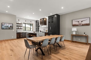 A modern kitchen with a wooden dining table and chairs, a built-in oven, and dark cabinets.