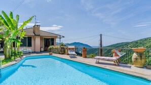 Ein Pool mit Liegestühlen, eine Steinmauer und Blick auf einen Berg.