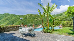 Eine Terrasse mit Steinboden, einem Pool und einem Tisch mit Stühlen.