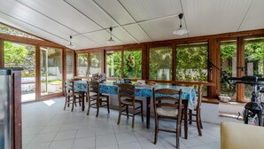 Ein Essbereich mit einem Tisch, gedeckt für sechs Personen, umgeben von Holzsesseln, großen Fenstern und einem Deckenventilator.
