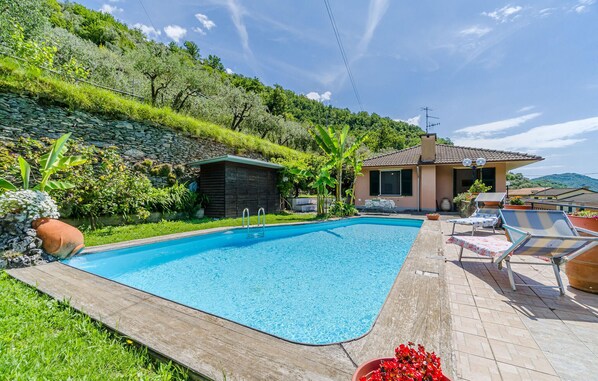 A swimming pool with a wooden deck, surrounded by lush greenery and a hillside. - Gorgeous home in Testana (Testana)