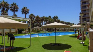 Ein Poolbereich mit Palmen, Sonnenschirmen und einem Gebäude im Hintergrund.