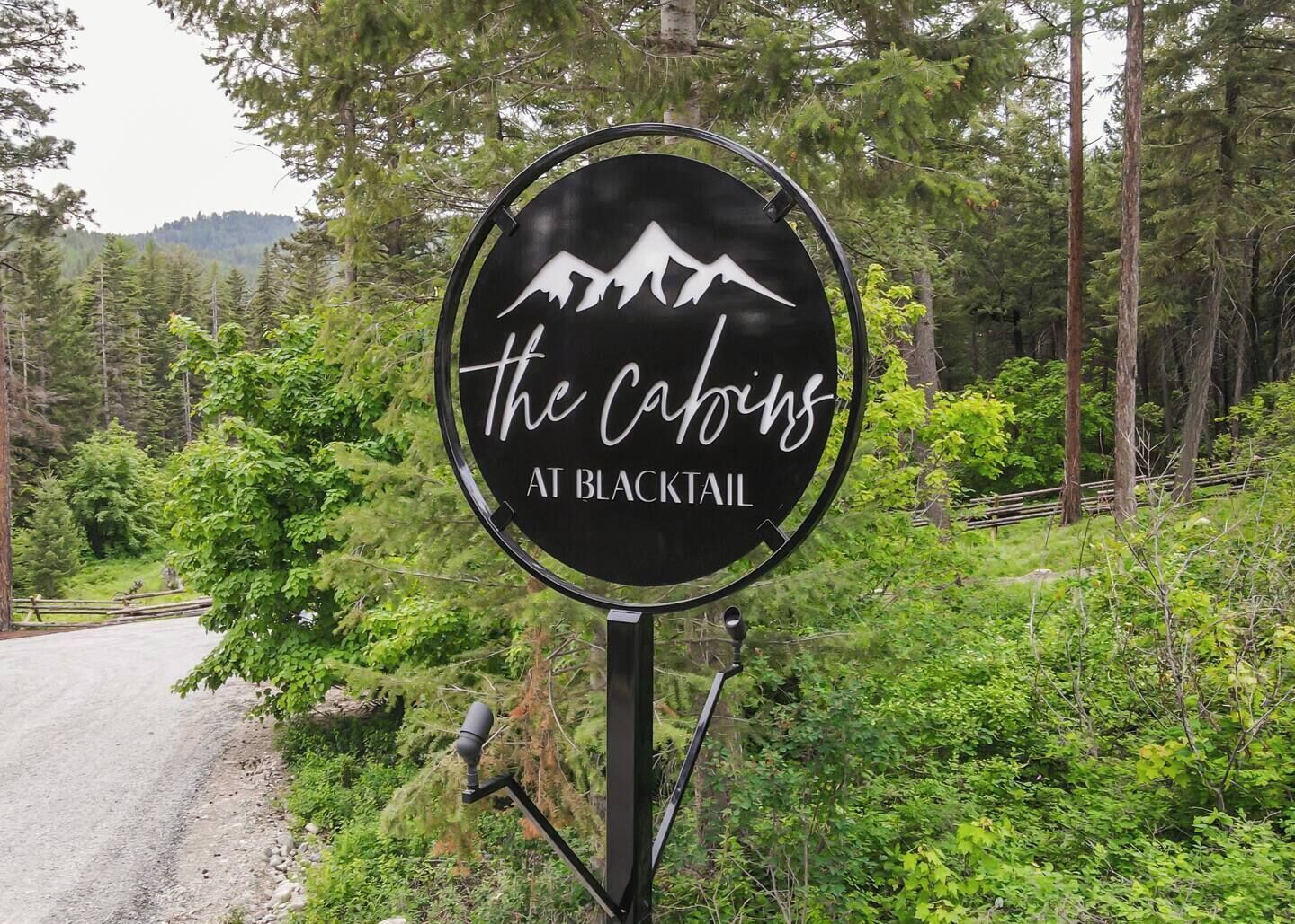 Ein rundes Schild mit dem Aufdruck 'the cabins at blacktail' inmitten eines bewaldeten Geländes.