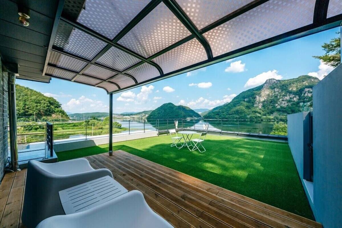 A modern room with a large window overlooking a scenic landscape, including mountains and a lake.