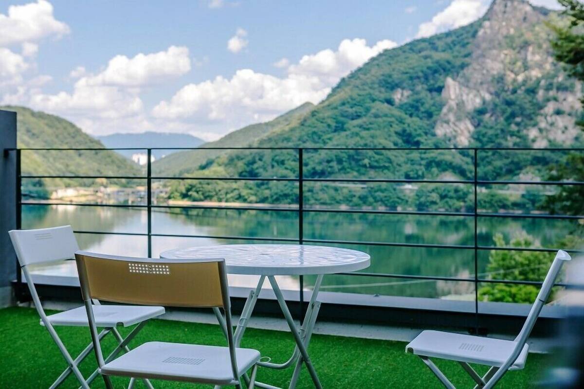 A balcony with a table and chairs overlooking a lake and mountains.