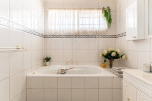Un baño moderno con una bañera independiente, una pequeña planta en maceta, un florero con flores y un perchero para toallas.