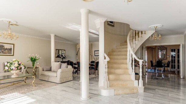 A spacious living room with a marble floor, a beige sofa, a glass coffee table, and a staircase with a white railing. - Comfort Private room with queen bed & study (Preston)