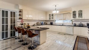 A modern kitchen with white cabinetry, a central island with bar stools, and a chandelier. - Comfort Private room with queen bed & study (Preston)