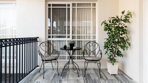 A balcony with two metal chairs and a small table, a potted plant, and a window with curtains. - Comfort Private room with queen bed & study (Preston)