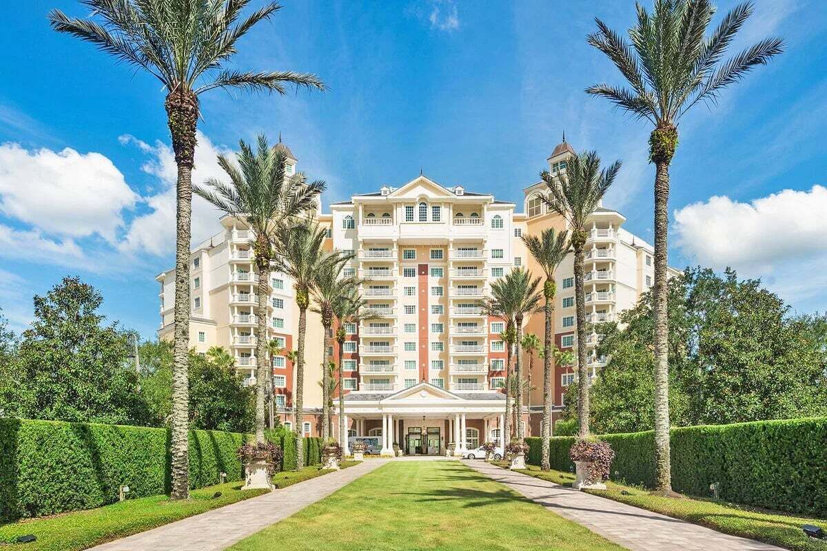 A multi-story hotel with a central entrance, surrounded by palm trees and well-maintained lawns.