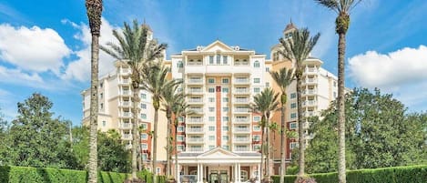 A multi-story hotel with a central entrance, surrounded by palm trees and well-maintained lawns.