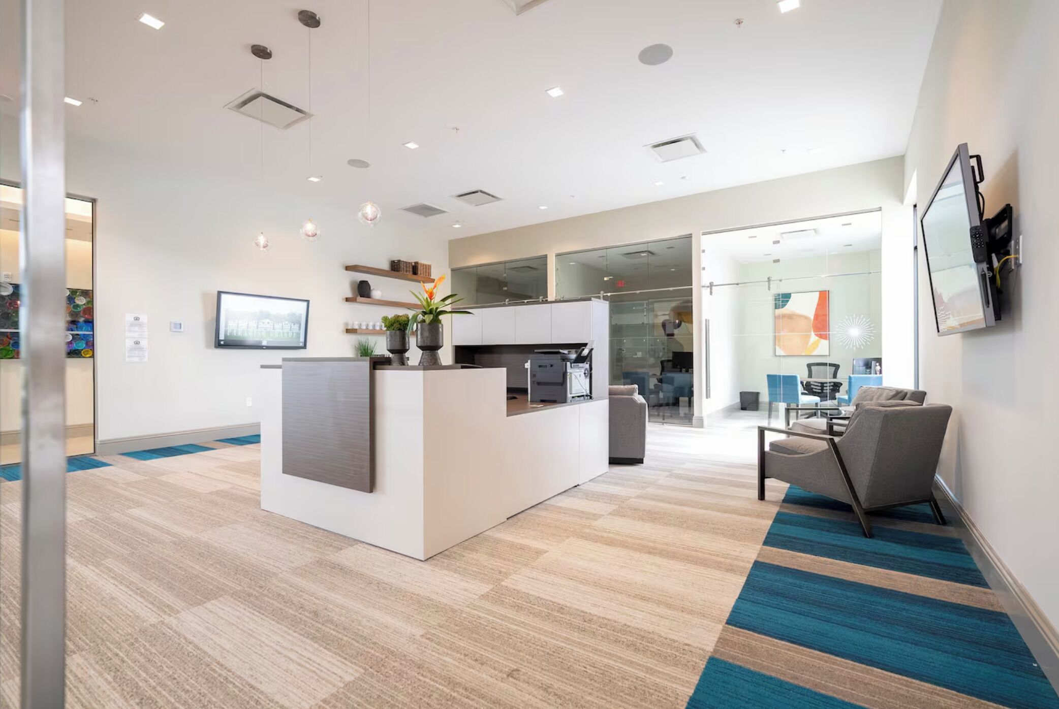 A modern reception area with a white desk, a flat-screen TV, and a potted plant.