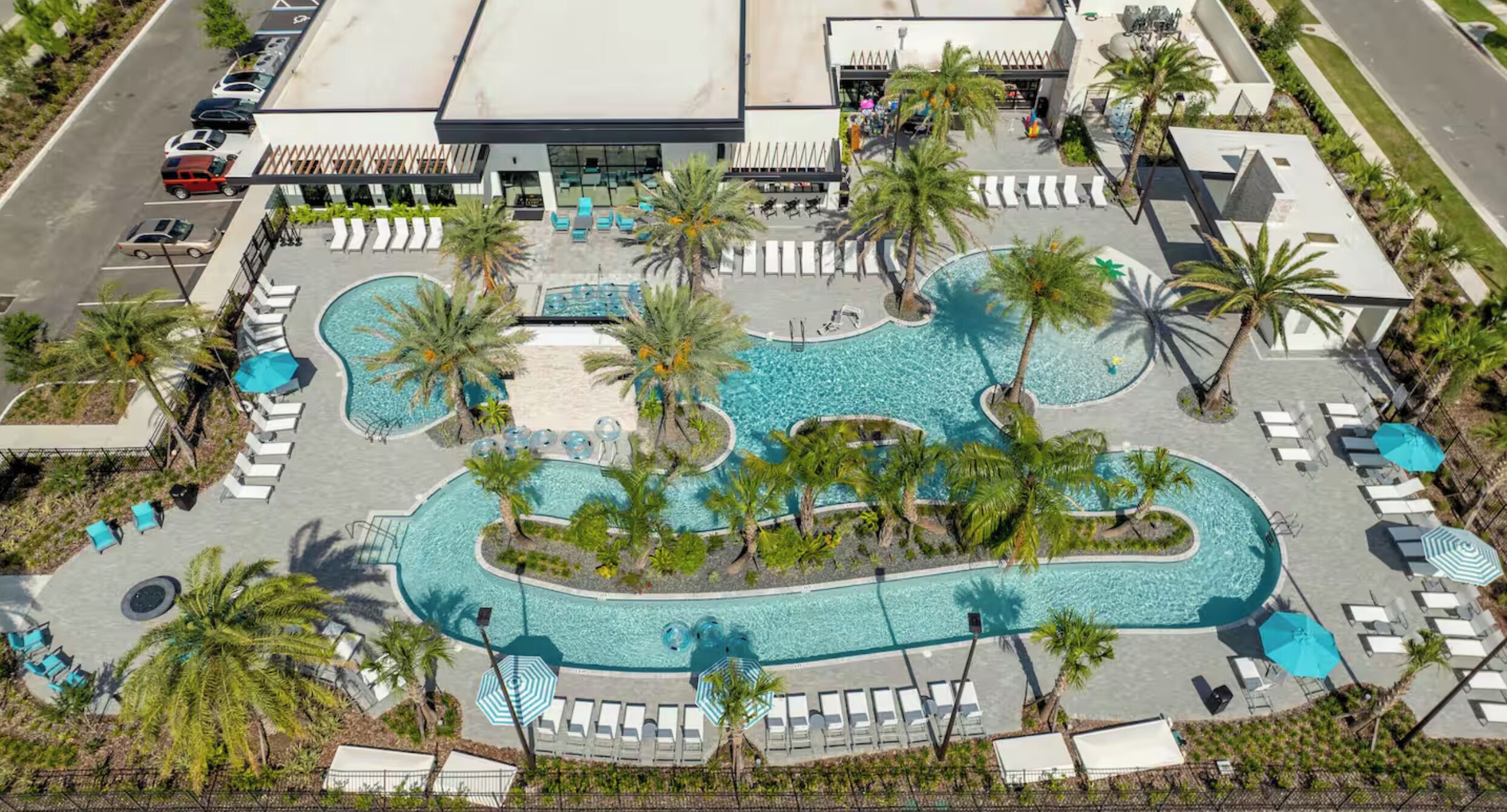 An aerial view of a resort with a central swimming pool, multiple lounge areas, and palm trees.