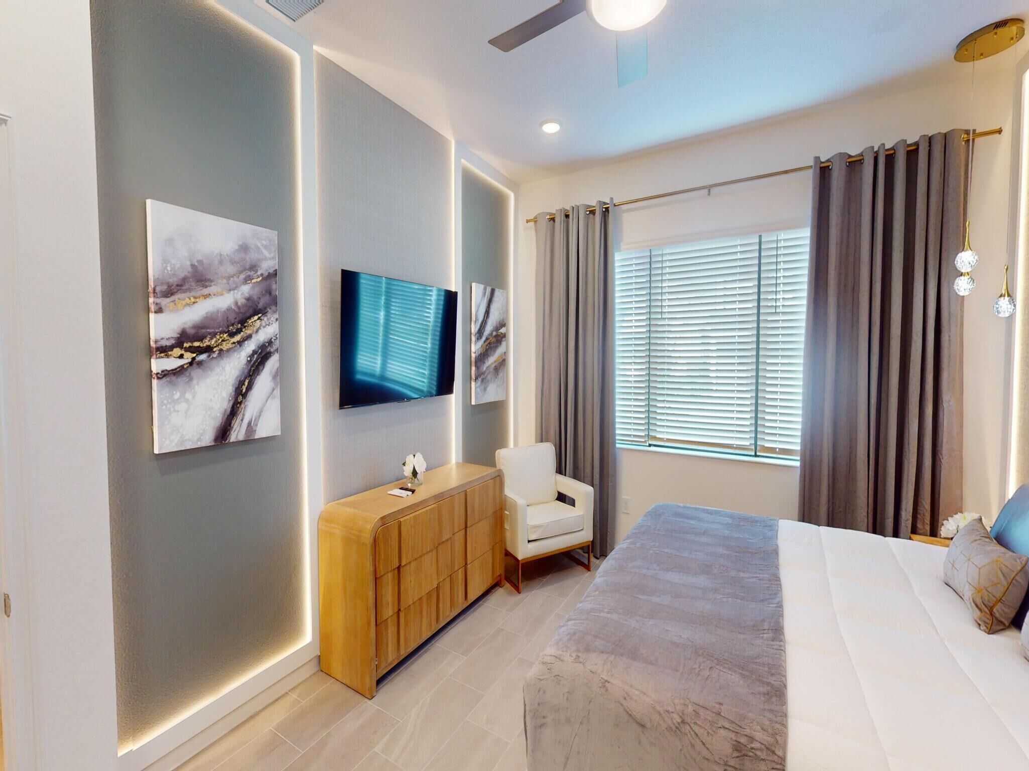 A modern bedroom with a large bed, a TV mounted on the wall, a wooden cabinet, and a chair.
