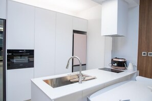 A modern kitchen with a built-in oven, a stainless steel sink, and a coffee maker. - The Beige (Geoje)